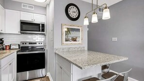 A compact kitchen with white cabinetry, a microwave, a stove, and a granite countertop. - Seawatch Condo | Marsh View & Pool  | Cozy 2BR  |  Relaxing Amenities Free Travel Insurance on weekly rentals (Murrells Inlet)