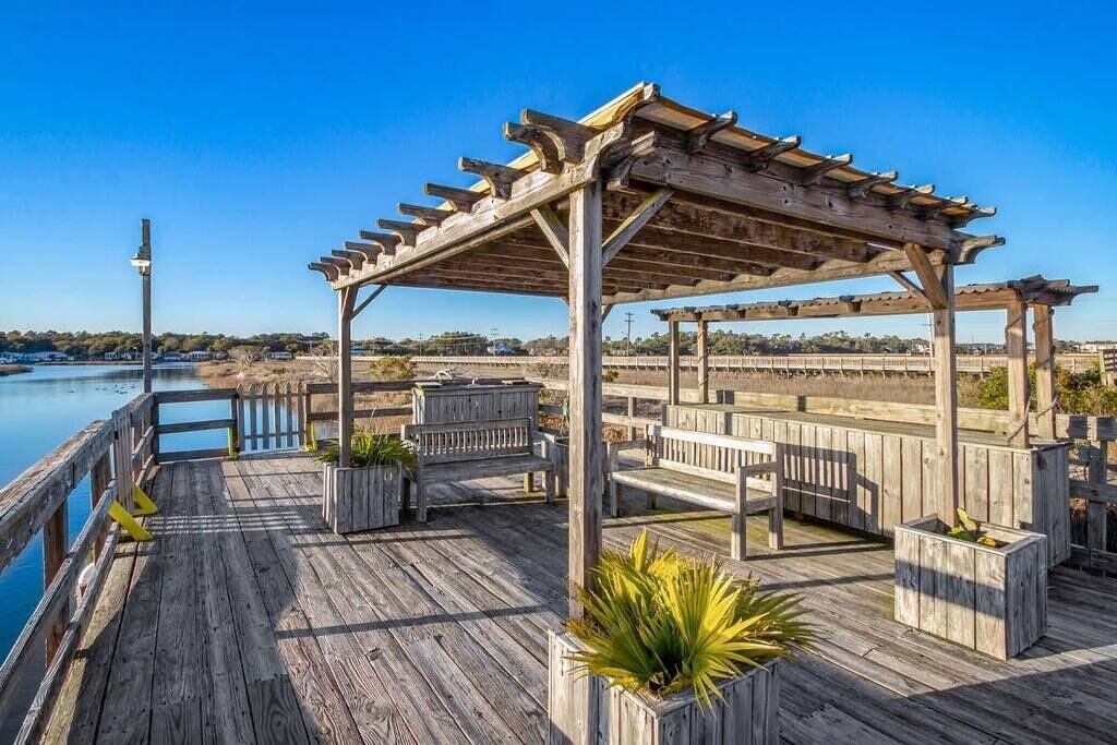 A wooden deck with a pergola, benches, and planters.