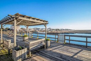 Une jetée en bois, agrémentée d’une pergola et de bancs, qui offre une vue sur une étendue d’eau calme et sur une côte lointaine parsemée de bâtiments.