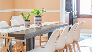 Un coin repas avec une longue table, des chaises blanches, deux vases décorés contenant des plantes et un set de table en fibres tressées.