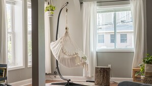Une pièce avec un fauteuil suspendu en macramé, un tabouret en bois et une plante en pot.