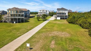 A residential area with multiple two-story houses, a central pathway, and a view of the ocean. - Rio Rodanthe | Oceanfront 8BR with Private Lazy River | Outer Banks, NC (Rodanthe)