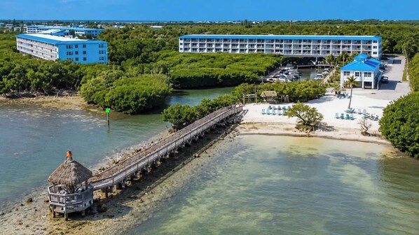 A coastal hotel with a pier, beach, and lush greenery.