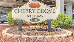 A sign for Cherry Grove Villas, number 200, with a decorative design and a sunset in the background. - Spacious 6BR Oceanview Condo w/ Pool & Hot Tub (North Myrtle Beach)