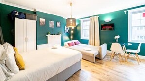 Une chambre moderne avec un grand lit, un bureau et une chaise. On y trouve une fenêtre avec des rideaux, un téléviseur fixé au mur et un luminaire au plafond.