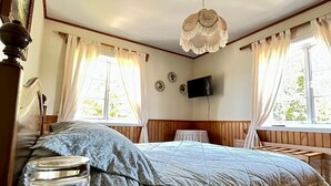 Un dormitorio con una cama, una mesa de madera con un tarro de vidrio, un mantel individual y una lámpara colgante.