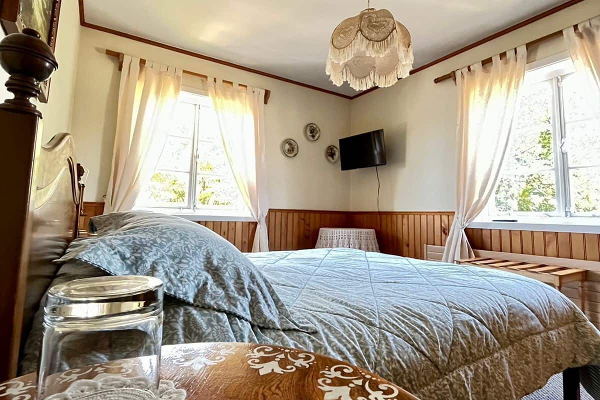 Un dormitorio con una cama, una mesa de madera con un tarro de vidrio, un mantel individual y una lámpara colgante.