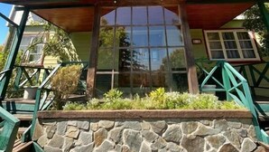 Una casa de dos pisos con base de piedra, una escalera de madera y un ventanal grande.