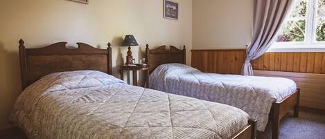 A room with two single beds, wooden headboards, a nightstand with a lamp, and framed pictures on the wall.