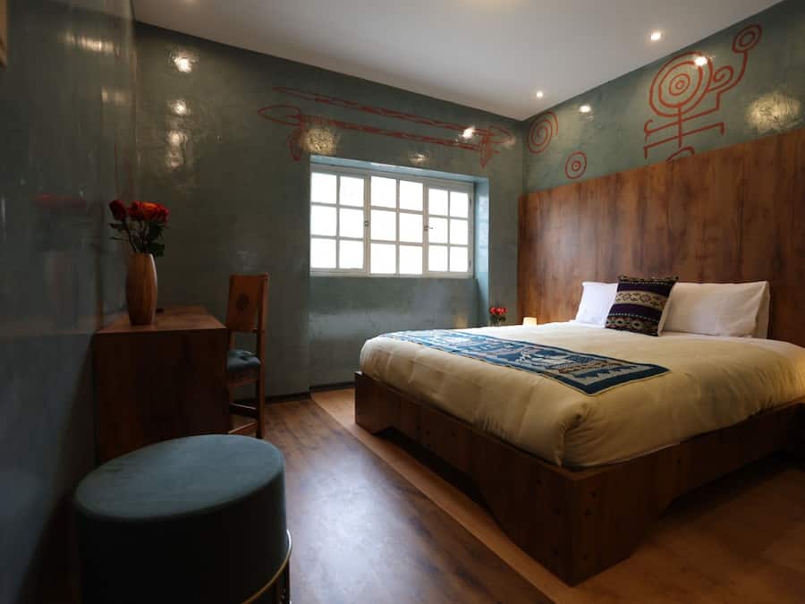 Un dormitorio con cabecera de madera, una cama grande, una ventana, un escritorio con silla y un jarrón con flores.