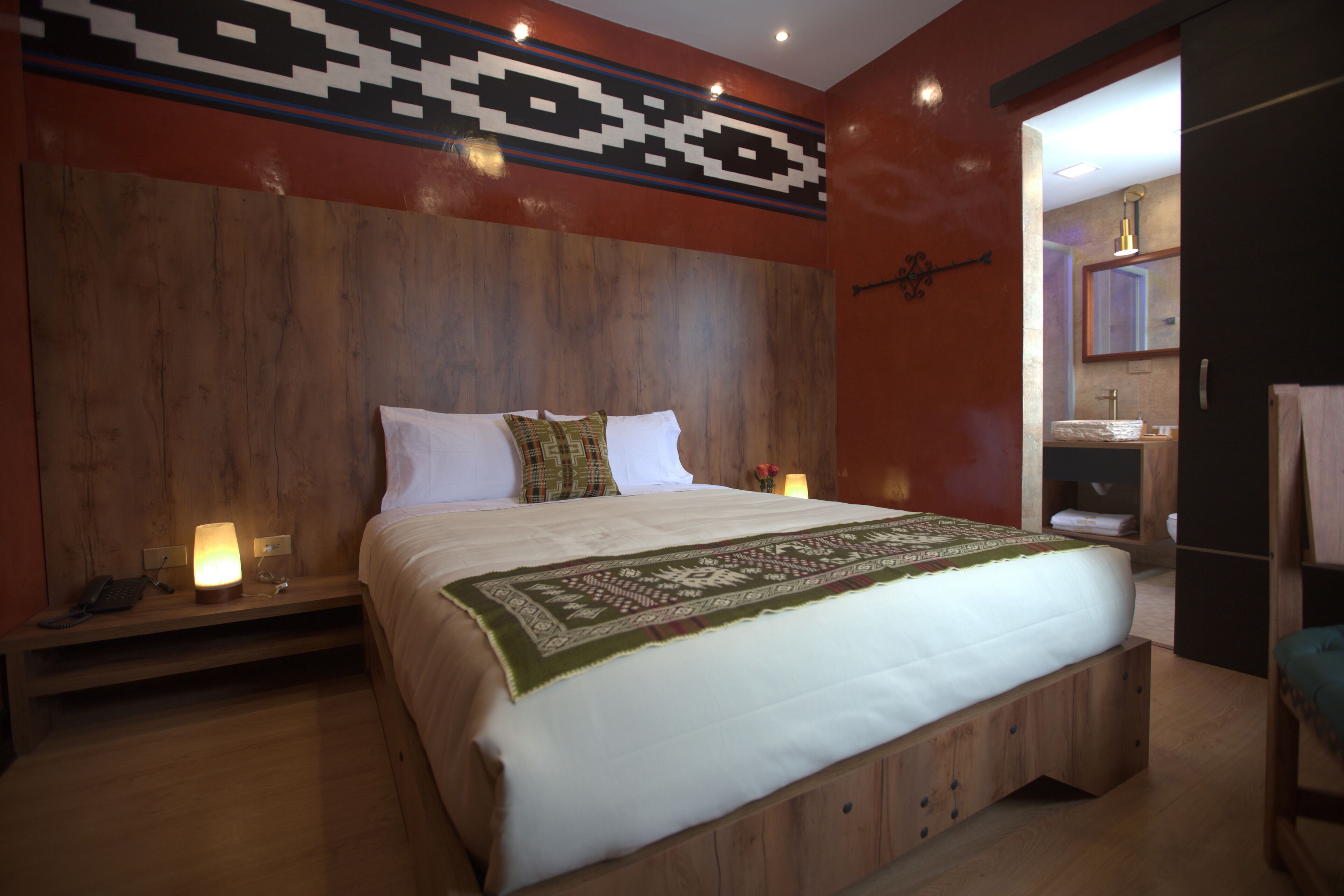 A modern hotel room with a large bed, wooden headboard, and a small bedside table with a lamp.