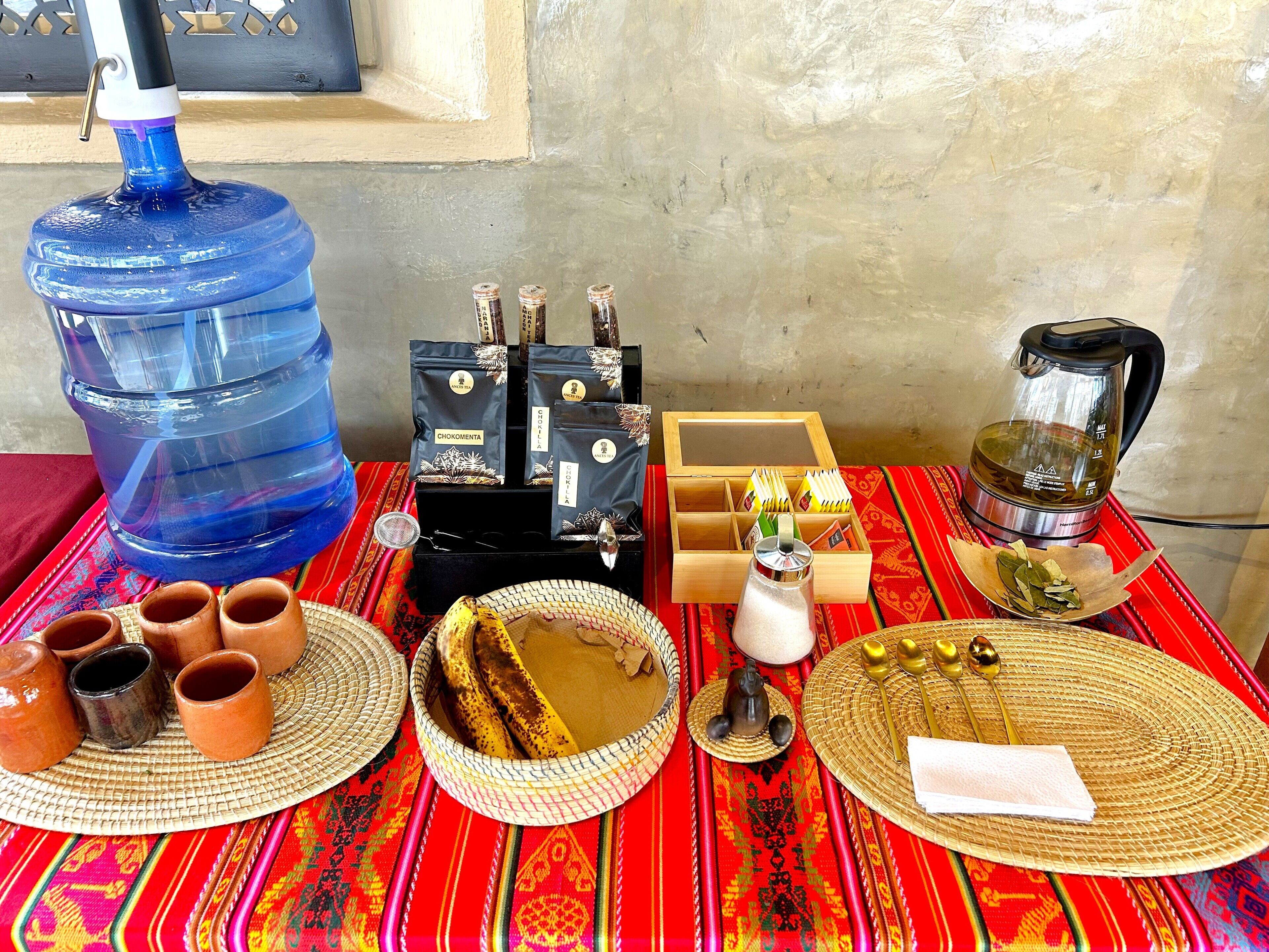 A table with a water dispenser, tea bags, a kettle, and traditional serving items.