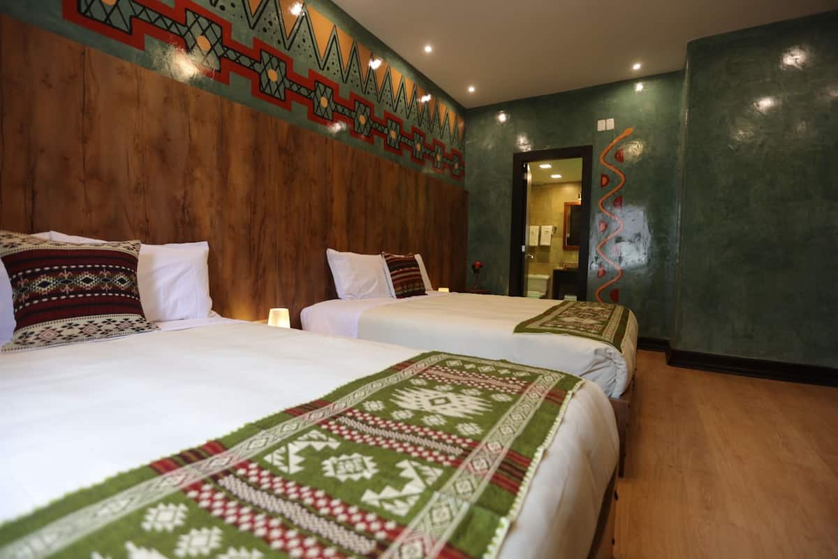 Une chambre d’hôtel avec deux lits, une tête de lit en bois, un décor mural à motifs et un miroir.