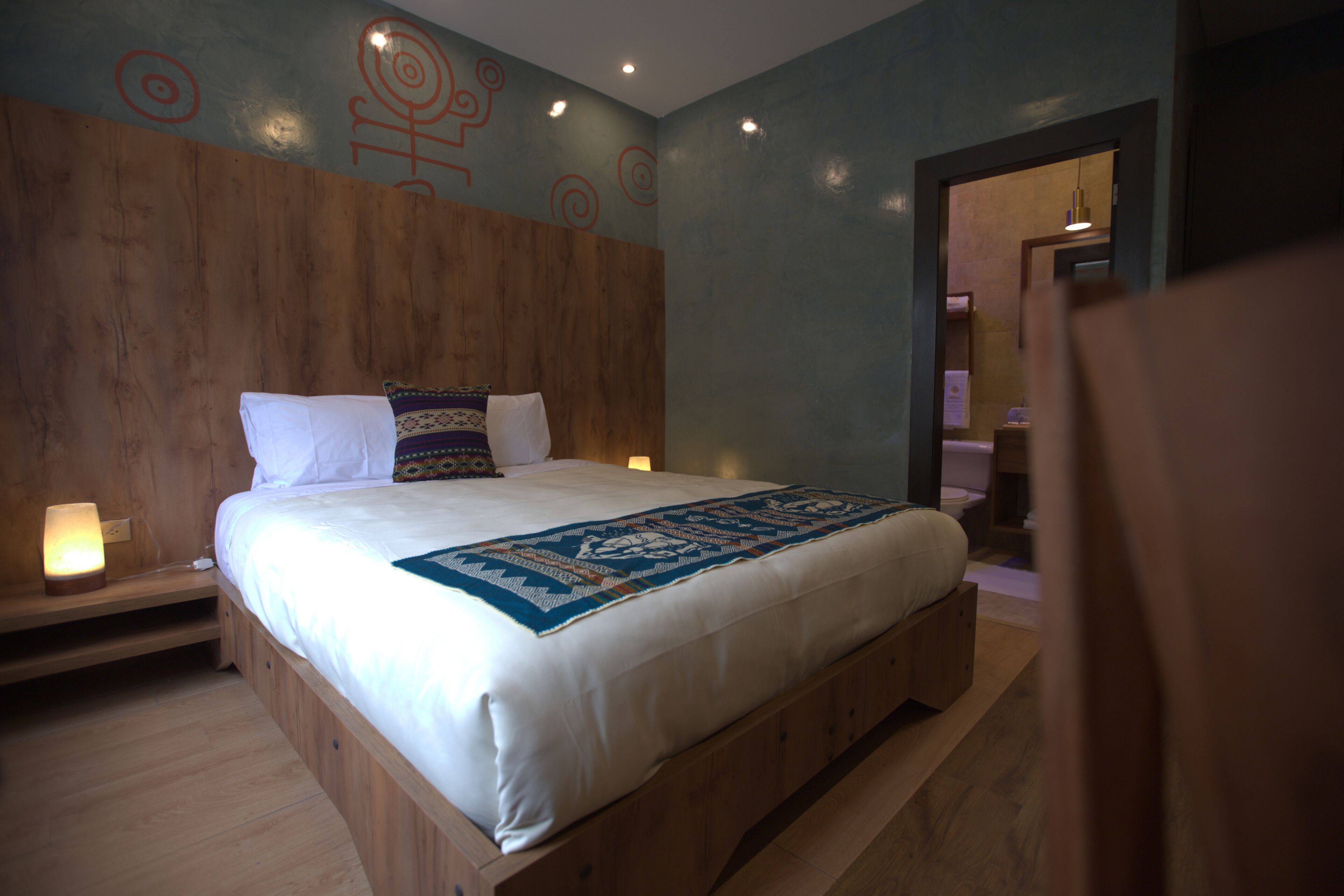 Un dormitorio con cabecera de madera, una cama grande con ropa blanca, un plaid azul estampada y una mesita de noche con lámpara.