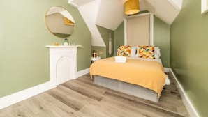 Une chambre à coucher avec un lit, un miroir rond, une table de chevet et une lampe fixée au mur.