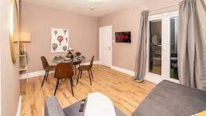 Un salon chaleureux comprenant un coin repas, un téléviseur fixé au mur et une porte-fenêtre coulissante donnant sur un balcon.