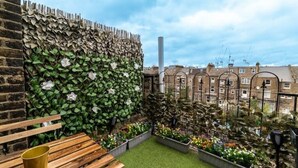 Un jardin sur le toit, avec un banc en bois, un mur de pierre recouvert de lierre et des jardinières fleuries.