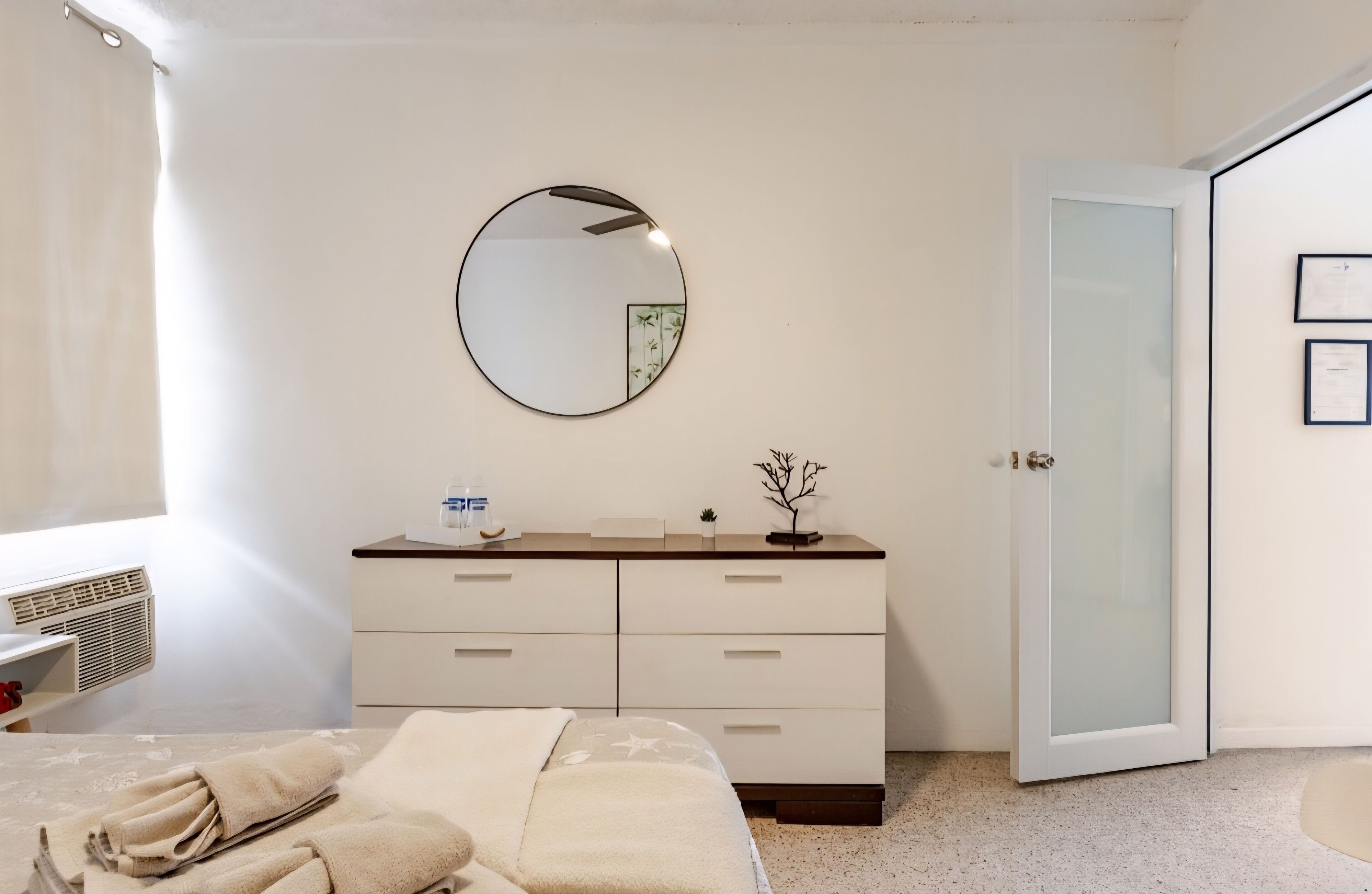 A bedroom with a bed, a bedside table, a dresser, a mirror, and a door.