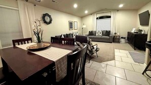 A dining area with a wooden table and chairs, a sofa, a TV, and a clock on the wall. - Vista Rental 1 Cozy Home, 25 min from Zion National Park (La Verkin)