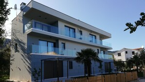 A modern two-story building with a flat roof, large windows, and a wooden fence. - 2 Bed House - Sleeps 4 - Garden - Parking - Wifi (Rasa)