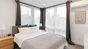 A modern hotel room with a large bed, a bedside table with a lamp, and a wall-mounted air conditioning unit. - Ravenna Trailside Retreat Walk to UW and U-Village (Seattle)