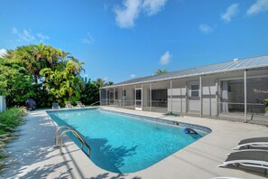 A swimming pool with a clear blue water, surrounded by a covered patio area with chairs and a covered structure. - Walk to the Beach, 4-bed / 2-bath / Heated Pool Home on Singer Island (West Palm Beach)