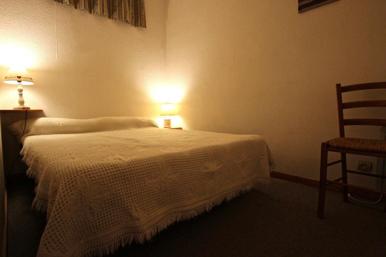 A bedroom with a bed, two bedside lamps, and a wooden chair.