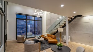 Een moderne woonkamer met een groot raam, een trap en eigentijds meubilair.