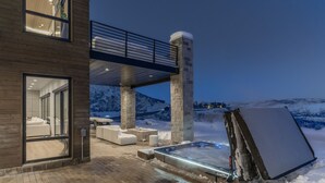 Een modern huis met een jacuzzi, buitenzitplaatsen en een balkon met uitzicht op een besneeuwd landschap.