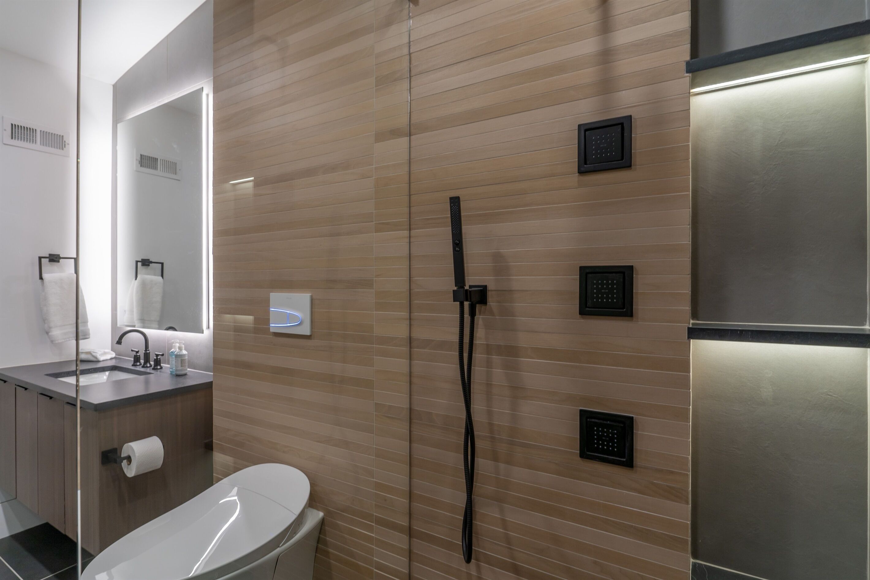 A modern bathroom with a wooden panel wall, a glass shower enclosure, a stainless steel sink, and a toilet.