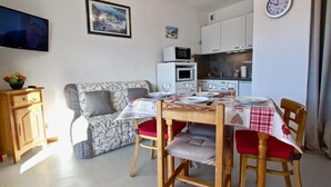 A cozy living room with a sofa, a dining table set for two, and a kitchen area with cabinets and a microwave. - 10m from ski slopes, 1st floor, balcony, tv, 22m², Chamrousse (Chamrousse)