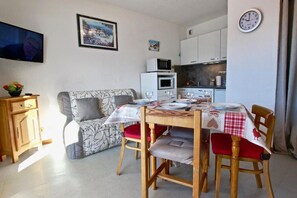 Ein gemütliches Wohnzimmer mit einer Couch, einem Esstisch für zwei Personen und einer Küchenzeile mit Schränken und einer Mikrowelle.