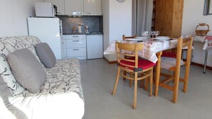 A compact living space with a kitchenette, a dining table set for two, and a sofa with cushions. - 10m from ski slopes, 1st floor, balcony, tv, 22m², Chamrousse (Chamrousse)