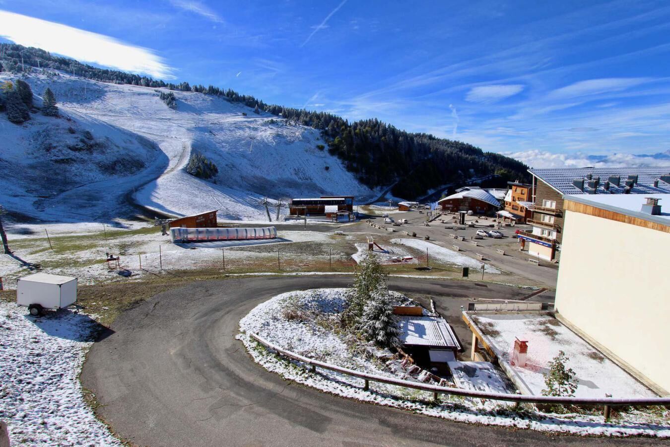A snow-covered parking area with buildings and a road curving through it.