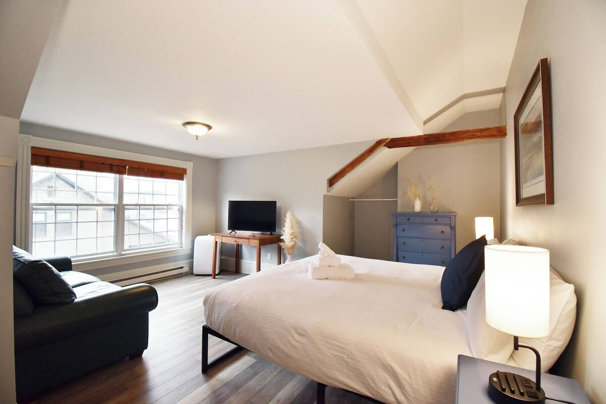 A bedroom with a bed, a desk, a television, and a dresser.