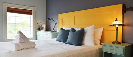 A neatly made bed with white linens and a folded towel, a bedside lamp, and a nightstand with a drawer.