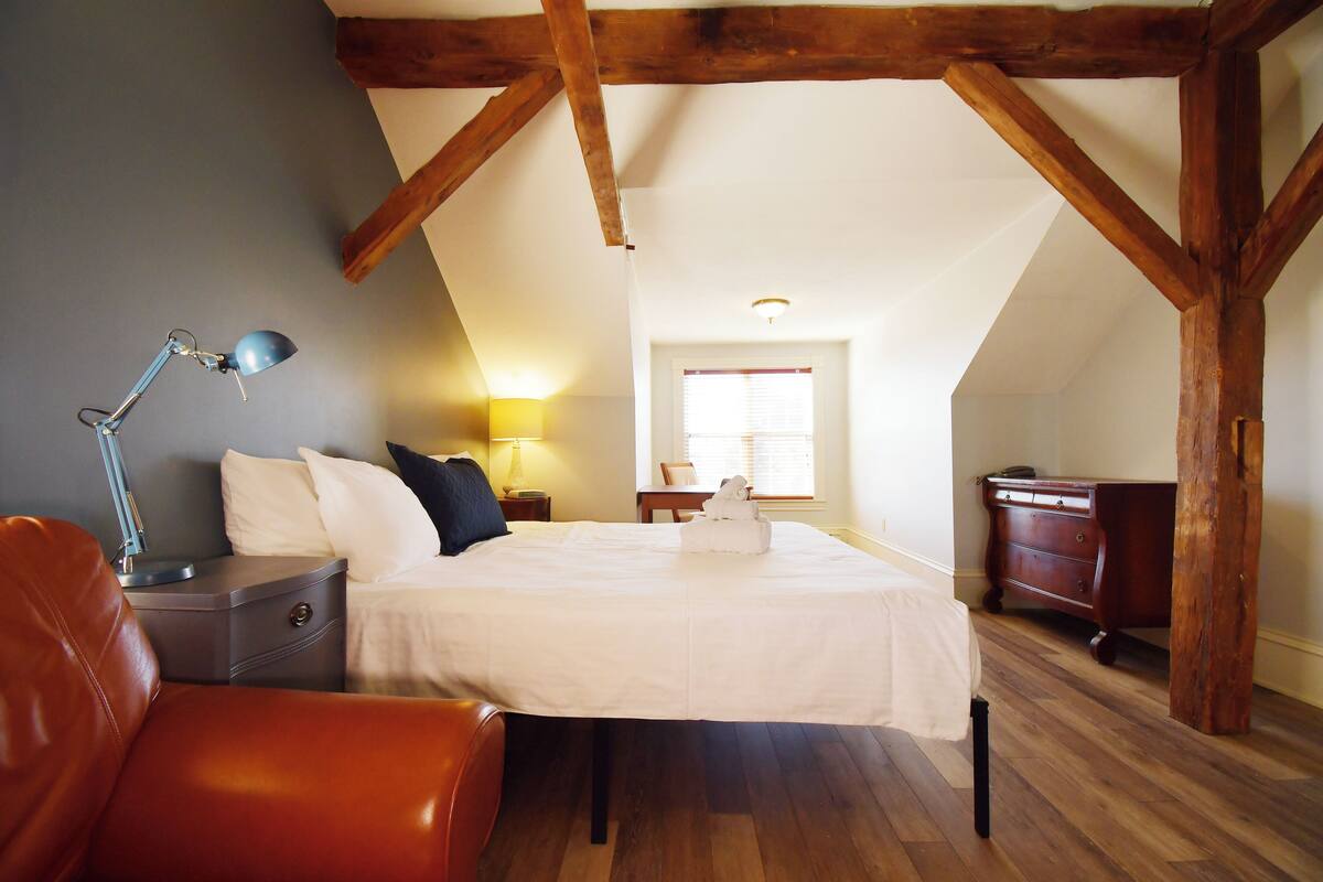 A bedroom with a bed, a nightstand, a desk, and a chair.