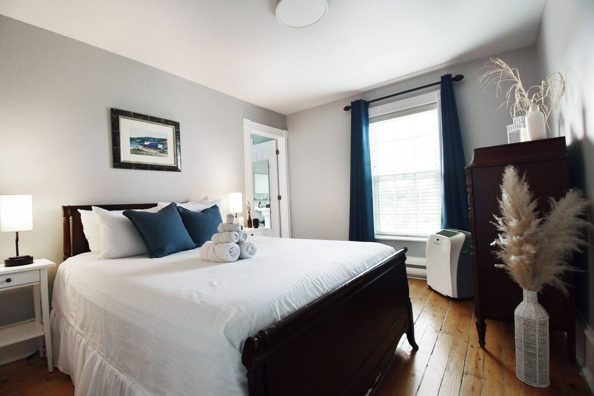 A neatly arranged bedroom with a bed, bedside tables, a dresser, and a window with curtains.