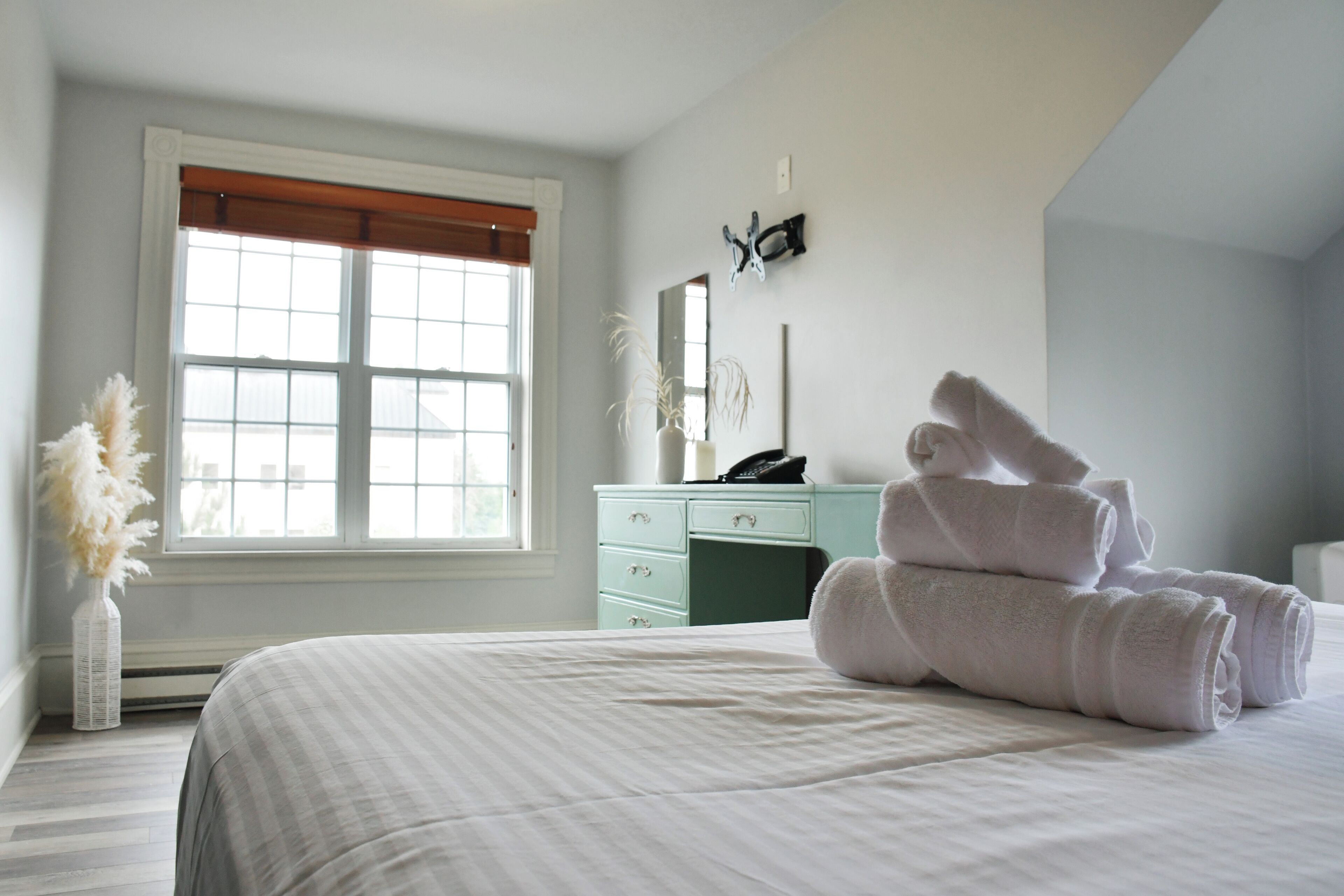 Une chambre avec un grand lit, une commode, une fenêtre avec des stores et un miroir au mur.