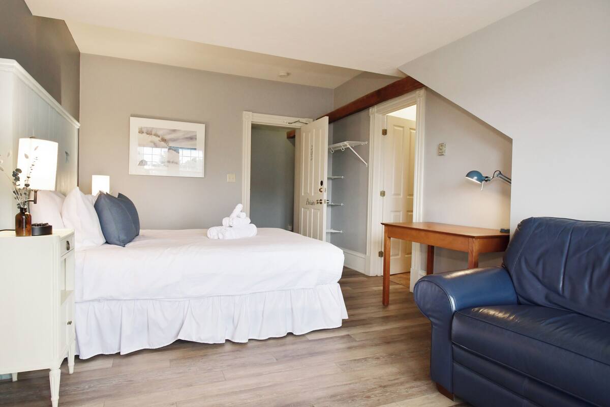 A bedroom with a bed, bedside table, lamp, and a blue sofa.