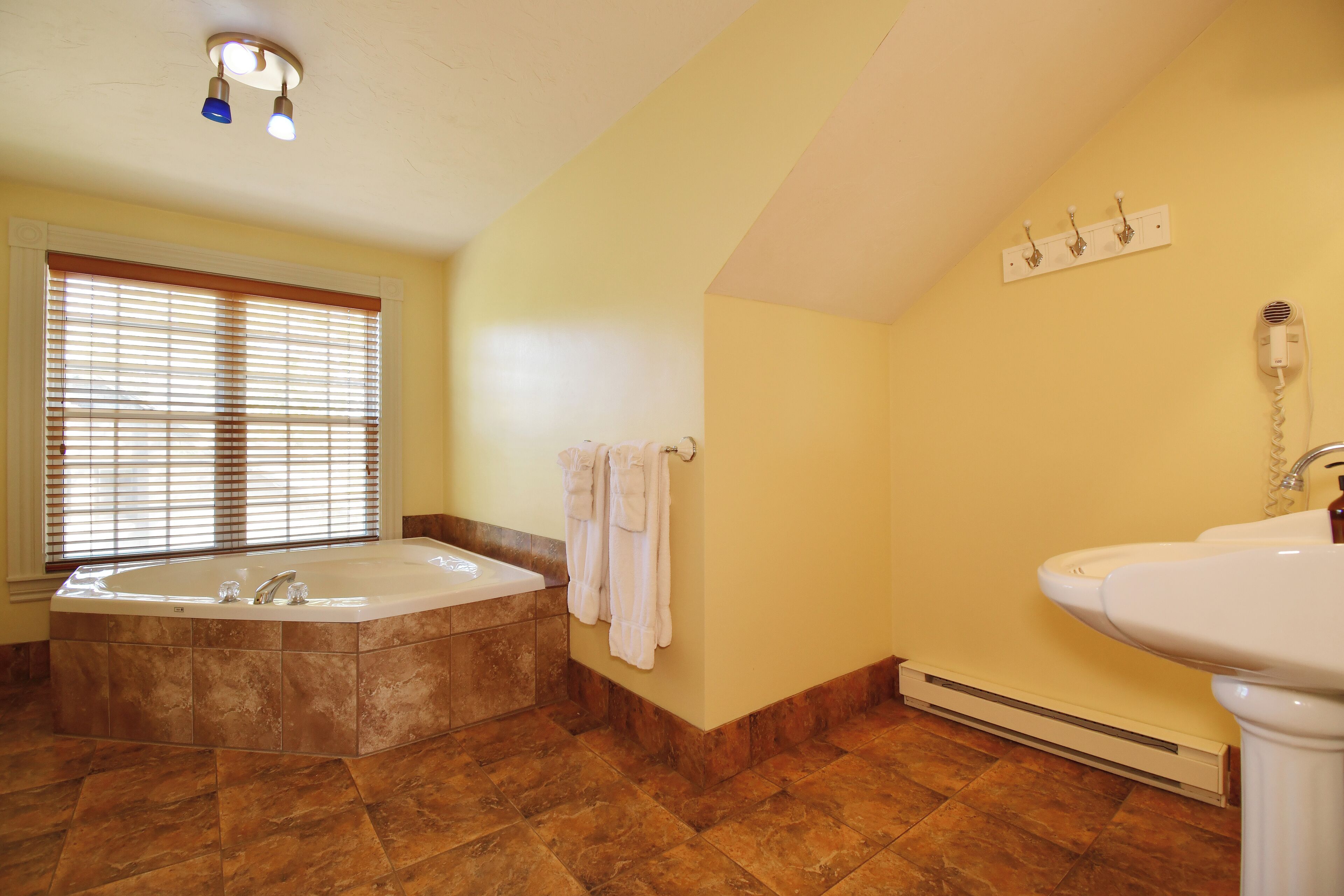 A bathroom with a large bathtub, a sink, and a window with blinds.