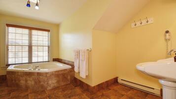 A bathroom with a large bathtub, a sink, and a window with blinds.