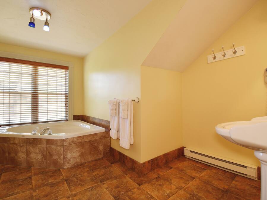 A bathroom with a large bathtub, a sink, and a window with blinds.