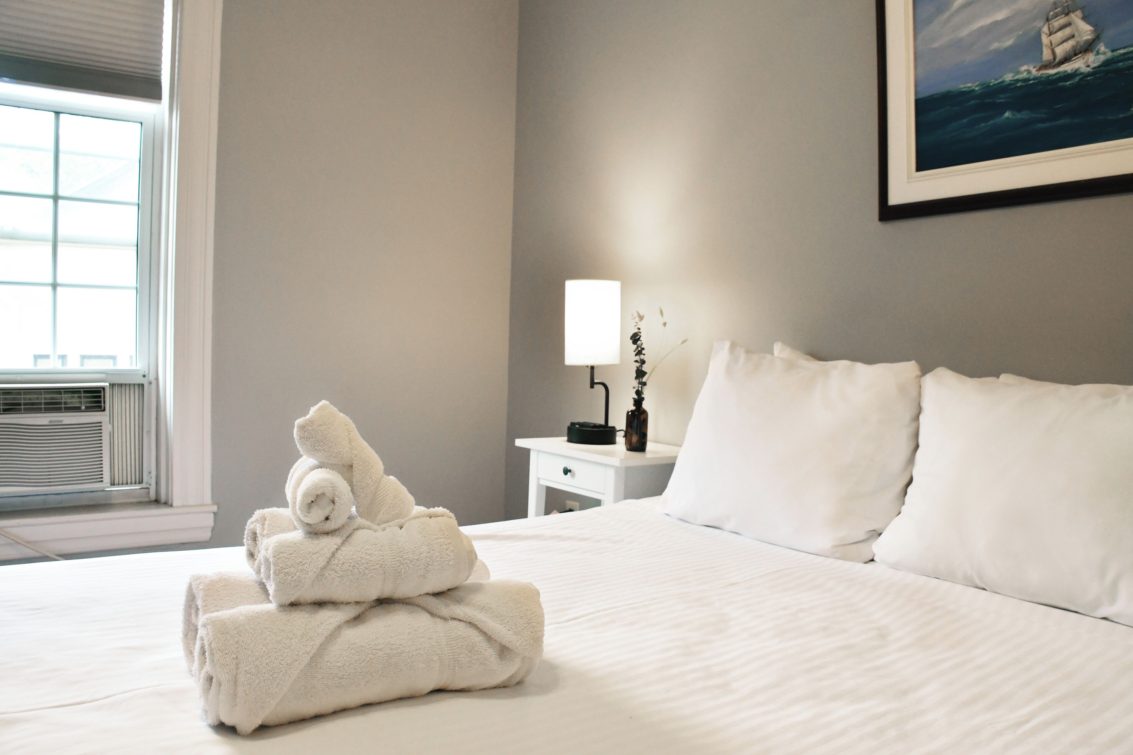 A neatly made bed with white linens, a bedside lamp, and a framed picture on the wall.