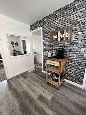 A room with a brick wall, a coffee machine, and a wooden cart.