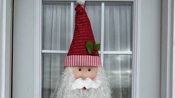 Una porta con un decorativo ornamento natalizio raffigurante Babbo Natale appeso sopra una finestra con tende bianche.