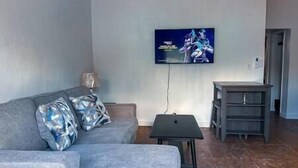 Un salon avec un canapé gris, une petite table et un téléviseur fixé au mur.