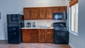 Une cuisine avec des meubles de rangement en bois, un réfrigérateur noir, un four à micro-ondes et une cuisinière.