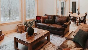 Amplia sala de estar con un techo de madera grande, varios ventanales, un sofá de cuero, una mesa de centro y un comedor.