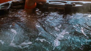 Una persona en un jacuzzi con vistas a árboles y un cielo nublado a través de amplias ventanas.